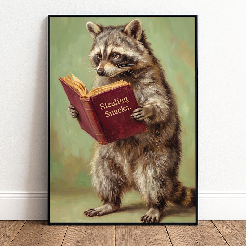 May include: A framed print featuring a raccoon reading a book with the text "Stealing Snacks." The raccoon is depicted in a realistic style with brown and gray fur, set against a green background. The book is a deep red color.