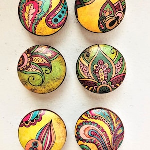 May include: Six round wooden knobs with a yellow background and colorful paisley designs. The knobs are approximately 2 inches in diameter.