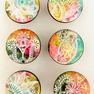 May include: Six round decorative cabinet knobs with colorful watercolor backgrounds and white floral designs. The knobs feature a variety of patterns, including paisley and floral motifs, with a dark brown edge.