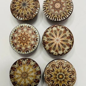 May include: Six round wooden knobs with intricate brown, beige, and white mandala designs. The knobs have a dark brown border.