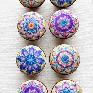 May include: Eight round wooden knobs with colorful mandala designs. The knobs feature intricate patterns in shades of blue, pink, yellow, and green.