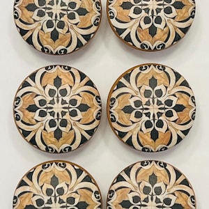 May include: A set of six circular wooden knobs, each featuring a symmetrical floral pattern in shades of tan, cream, and black. The design consists of repeating petal-like shapes radiating from the center, creating a detailed, intricate motif.