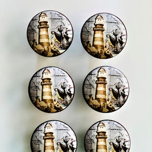 May include: Six round, wooden knobs with a nautical theme. Each knob features a lighthouse with a striped design, a ship with sails, and a vintage map background.