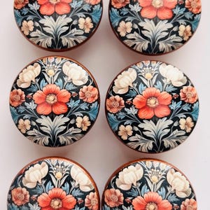 May include: Six round cabinet knobs with a floral design. Each knob features a central red flower surrounded by smaller peach and white flowers, blue leaves, and a dark background. The knobs have a wooden edge.
