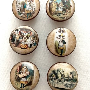 May include: Six round, wooden, decorative drawer knobs with a brown border. Each knob features a different illustration from Alice in Wonderland, including Alice with a pig, Alice with a cat, Alice with a Gryphon, Alice with the Mad Hatter, Alice with the Queen of Hearts, and Alice with the Cheshire Cat.