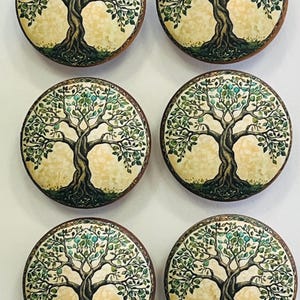 May include: Six round decorative objects featuring a tree design. Each object has a brown border, a cream-colored background, and a detailed tree illustration with green leaves and a dark trunk. The objects are arranged in a grid.