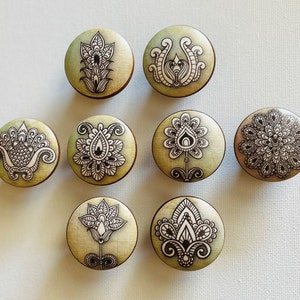 May include: Eight round wooden knobs with a green background and black and white floral designs. The knobs have a distressed look and are perfect for adding a touch of vintage charm to any home decor project.