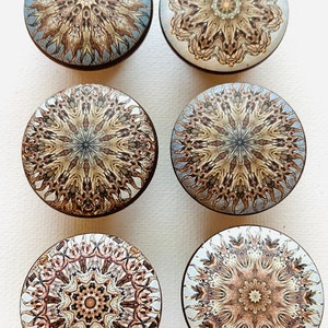 May include: Six round, decorative cabinet knobs with a mandala design. The knobs are made of wood and have a brown finish. The mandala designs are in shades of brown, gold, and white.