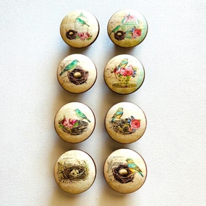 May include: Eight round wooden knobs with a vintage bird and nest design. Each knob features a different bird and nest scene with blue birds, eggs, and floral accents.