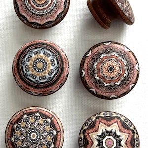 May include: Six decorative cabinet knobs with intricate mandala designs in shades of brown, pink, and white. The knobs are made of wood and have a round shape.