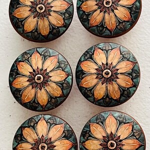 May include: A set of six circular wooden knobs, each featuring a detailed floral pattern with orange and yellow petals radiating from a dark brown center, set against a dark teal and black background with a smooth, polished finish.