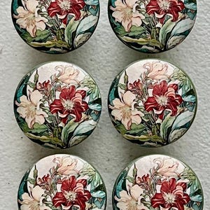 May include: Six round decorative cabinet knobs with a floral design. Each knob features a central cluster of red and cream-colored flowers surrounded by green leaves and a white background. The knobs are approximately 1.5 inches in diameter.