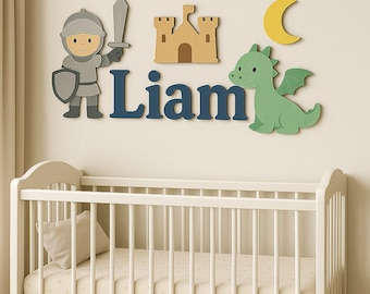 May include: Wooden wall decor featuring a knight, castle, dragon, and crescent moon. The name "Liam" is spelled out in blue letters. The decor is above a white crib with a beige mattress and pillow.