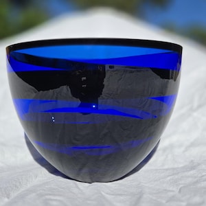 May include: A striking, hand-blown glass bowl with a deep cobalt blue and black striped design. The bowl has a rounded shape and a smooth, glossy finish. The bowl is approximately 6 inches wide and 4 inches tall.