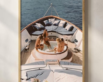 May include: A framed print showing a yacht with people in a hot tub. The yacht has blue cushions and wooden decking. The image captures a relaxing scene on the water. The print is framed in a gold-coloured frame, adding a touch of elegance to the artwork.