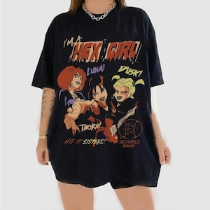 May include: A black short-sleeve t-shirt featuring a graphic print of the Hex Girls band members Luna, Thorn, and Dusk. The text reads I'M A HEX GIRL, LUNA, DUSK, THORN, HIT IT SISTERS, and HEXGIRLS SCOOBY-DOO in various colors and fonts across the front.
