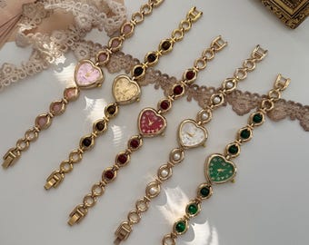 May include: Five gold-toned heart-shaped watches with various colored faces and beaded bands. The watch faces are pink, gold, red, white, and green. The bands feature a chain link design with alternating colored beads.