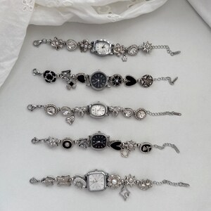 Peut inclure: Cinq bracelets à breloques argentés avec de petits cadrans de montre. Chaque bracelet présente divers charms, notamment des fleurs, des cœurs et des formes géométriques. Les cadrans de montre ont différentes formes et couleurs, avec des affichages analogiques et numériques.