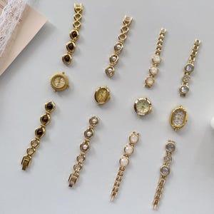 May include: An assortment of vintage gold-toned watches and watch bands. The watches have round and oval faces with various designs. The watch bands feature decorative elements like pearls, crystals, and brown stones.