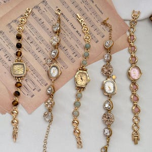 Peut inclure: Cinq montres-bracelets de style vintage, de couleur dorée, avec divers éléments décoratifs. Chaque montre présente une forme de cadran différente et est ornée de pierres précieuses, de perles et de breloques. Les bracelets sont liés avec des accents décoratifs.