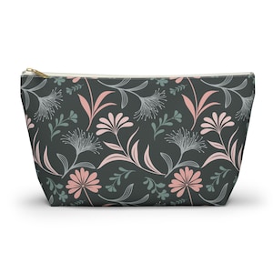 May include: A zippered pouch with a floral pattern. The dark gray fabric is covered with a repeating design of pink, gray, and teal flowers and leaves. The zipper is gold-colored.