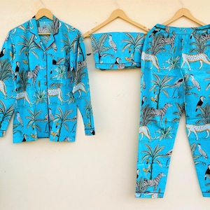 May include: A light blue pajama set with a jungle animal print. The set includes a button-down shirt and pants, both featuring zebras, leopards, toucans, and palm trees. The pajamas are displayed on wooden hangers.