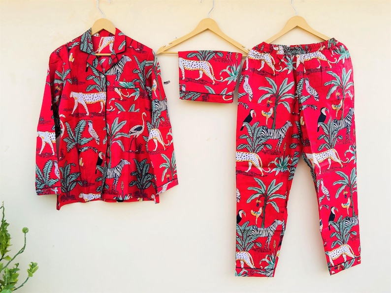May include: Red pajama set with a jungle animal print, including zebras, leopards, and birds. The set includes a button-down shirt, shorts, and pants, all hanging on wooden hangers. The fabric features a vibrant red background.