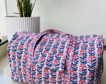 May include: A quilted travel bag with a floral pattern in pink, blue, and white. The bag has a rectangular shape with a zipper closure and two handles. The bag is approximately 20 inches long.
