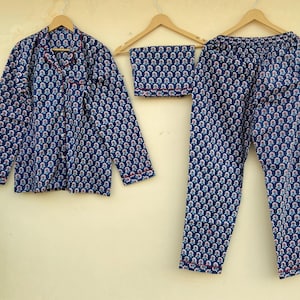 May include: A blue pajama set with a repeating floral pattern in white and pink. The set includes a button-down shirt, pants, and a folded sleep mask. The edges of the shirt and pants are trimmed with red piping.