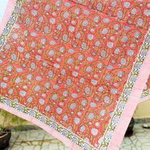 May include: A square textile featuring a vibrant coral-pink background with a repeating pattern of white pomegranate-like fruits, green leafy vines, and small white flowers. The fabric is framed by a border of thin white and coral-pink stripes.