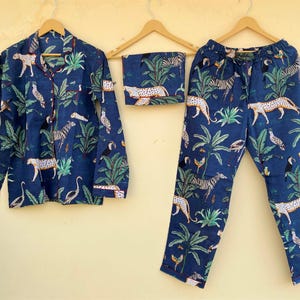 May include: A navy blue pajama set with a jungle animal print. The set includes a button-down shirt, pants, and a matching eye mask. The print features zebras, leopards, birds, and tropical plants.