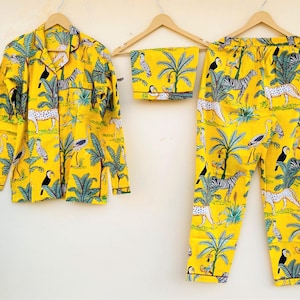 May include: Yellow pajama set with a jungle animal print, including zebras, leopards, and toucans. The set includes a button-down shirt, shorts, and pants, all hanging on wooden hangers against a white wall.