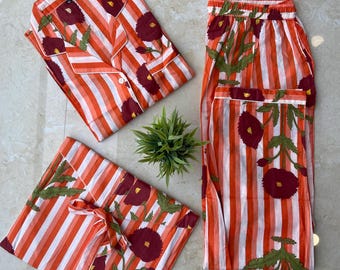 May include: A set of orange and white striped pajamas with a floral pattern. The set includes a button-down shirt, pants, and a matching bag. The floral design features burgundy flowers and green leaves.