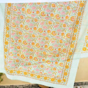 May include: A rectangular textile featuring a light green background with a repeating floral pattern of pink and yellow flowers and green leaves. The fabric is bordered by a wide band of yellow sunflowers and thin light green stripes.
