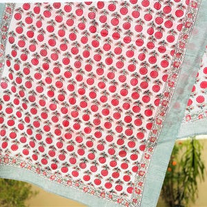 May include: A white fabric textile featuring a repeating pattern of small pink circular floral motifs with green stems. The fabric is bordered by a thin, light green and white striped edge, framed by a decorative floral vine border pattern.