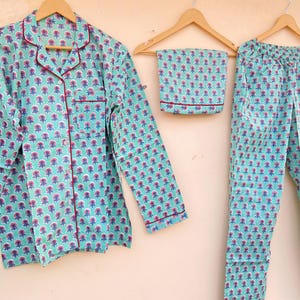 May include: A three-piece pajama set in a floral pattern. The set includes a long-sleeved button-down shirt, pants, and a matching eye mask. The pajamas are light blue with a repeating pattern of pink and blue flowers, and red trim.