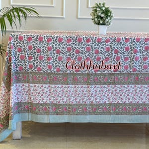 May include: A rectangular tablecloth featuring a white base with repeating pink floral patterns, green vine motifs, and horizontal striped borders in light blue and green. The text clothhubart is printed in the center of the fabric design.