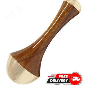 Puede incluir: Una herramienta de masaje de madera con un acabado pulido de color marrón oscuro y extremos de metal dorado. La herramienta tiene un diseño curvo y ergonómico, probablemente para el trabajo corporal o la masoterapia. La imagen también incluye un gráfico de "ENTREGA GRATUITA".