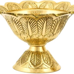 May include: A gold-colored, decorative bowl with a scalloped rim and a pedestal base. The bowl features intricate leaf-like patterns etched into its surface, creating a detailed and ornate design. The bowl is likely made of brass or a similar metal.