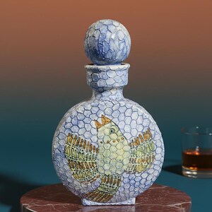 May include: A decorative, round bottle with a matching stopper. The bottle is light blue with a textured pattern and features a detailed bird design in yellow, green, and brown. The bottle sits on a red marble base.