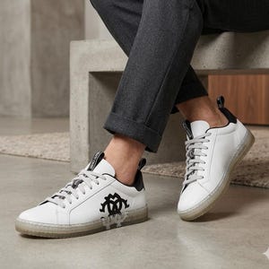 May include: White leather sneakers with black accents and a transparent sole. The sneakers feature a black logo on the side and gray laces. The shoes are designed for casual wear.