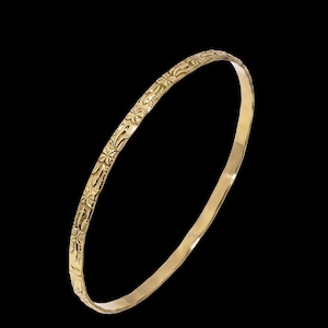 May include: A gold-coloured bangle bracelet with an intricate floral pattern. The bracelet is circular and appears to be made of metal. The design features repeating star-like shapes and other decorative elements. The background is black.