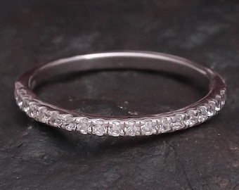 Puede incluir: Un anillo de banda de metal plateado fino que presenta una hilera de pequeñas piedras transparentes de corte redondo engastadas a lo largo de la mitad frontal de la banda. El anillo tiene un acabado pulido y un perfil delgado y elegante.