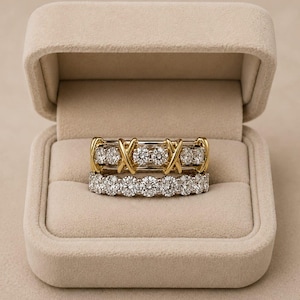 Peut inclure: Une paire de bagues empilées dans un écrin en velours beige. La bague supérieure présente un motif en forme de X doré alternant avec des pierres rondes transparentes. La bague inférieure est un anneau serti d'une rangée de pierres rondes.