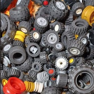 May include: A close-up shot of a pile of various toy tires and wheels. The tires are primarily black with gray or white rims, and some have visible tread patterns. Several yellow and red wheel components are also present, creating a colorful assortment.