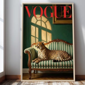 Op de afbeelding: Een ingelijste print met een cheetah die rust op een groen en wit gestreepte bank. Het woord "VOGUE" staat in het rood bovenaan. De achtergrond is een donkergroene muur met raamschaduwen.