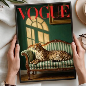 Op de afbeelding: Een ingelijste kunstdruk met een cheetah op een groen en wit gestreepte bank. Het rode woord "VOGUE" is prominent aanwezig. De print bevat ook de tekst "Fine Art Print" en "Premium Archival Quality Paper".