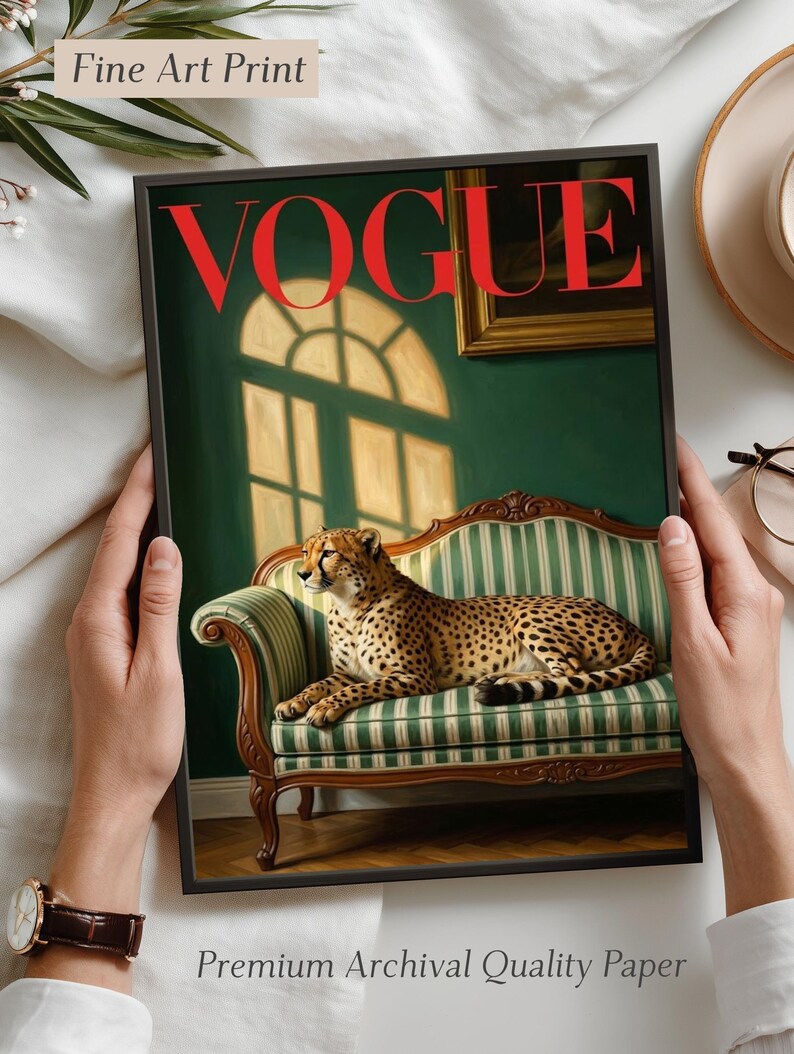Op de afbeelding: Een ingelijste kunstdruk met een cheetah op een groen en wit gestreepte bank. Het rode woord "VOGUE" is prominent aanwezig. De print bevat ook de tekst "Fine Art Print" en "Premium Archival Quality Paper".