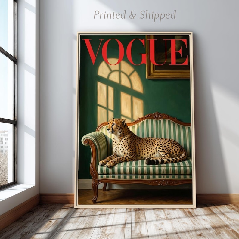 Op de afbeelding: Een ingelijste print met een cheetah die rust op een groen en wit gestreepte bank. Het woord "VOGUE" staat in het rood bovenaan. De achtergrond is een donkergroene muur met raamschaduwen.