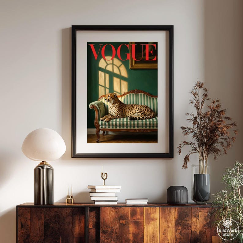Op de afbeelding: Ingelijste kunstprint met een cheetah op een groen en wit gestreepte bank. Het rode woord "VOGUE" staat bovenaan. De achtergrond toont een groene muur, een raam en een schilderij. Stijlvolle woondecoratie.